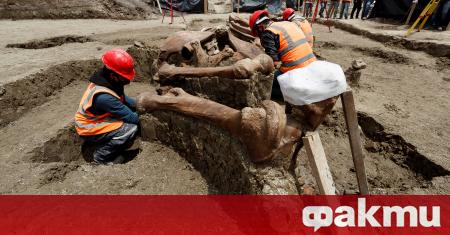 Археолози с каски и маски за лице внимателно отстраняват земята